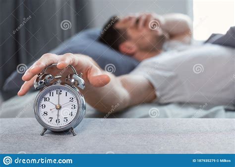 Sleepy Man Turning Off Alarm Clock Waking Up In Bed Indoors Stock Image