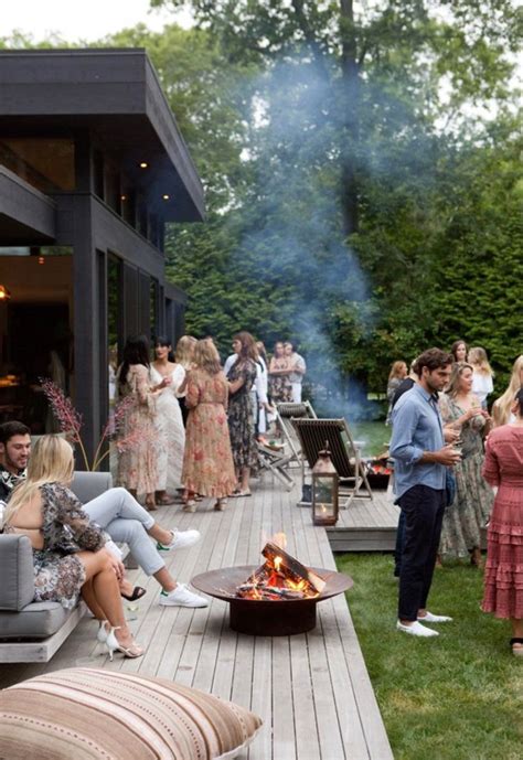 A Group Of People Gathered Around A Fire Pit On A Deck With Couches And