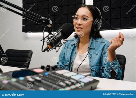 Young Female Radio Host Using Microphone And Headphones In Studio Stock