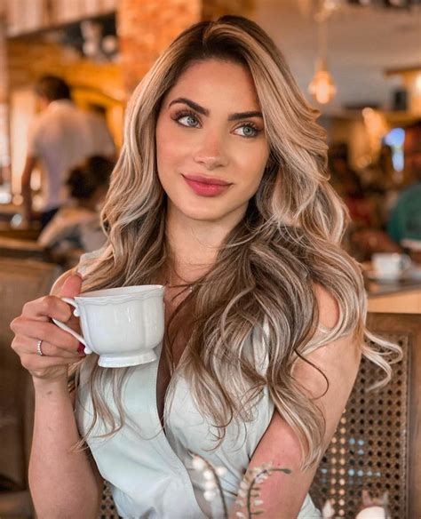 A Woman Sitting At A Table With A Cup In Her Hand