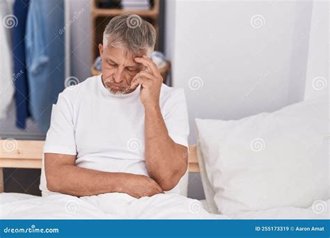 Middle Age Grey Haired Man Stressed Sitting On Bed At Bedroom Stock