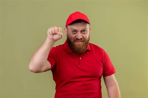 Jovem barbudo entregador de uniforme vermelho e boné levantando o punho