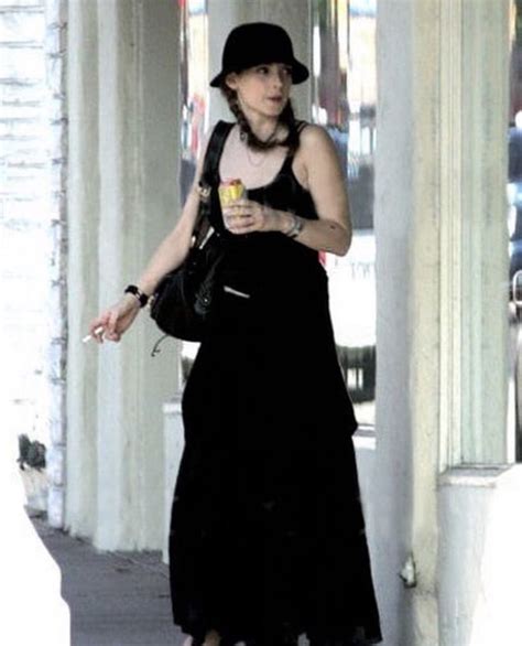 A Woman In Black Dress And Hat Walking Down The Street