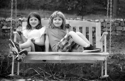 Portrait Of Brother And Sister Swinging On Swing In Summer Park