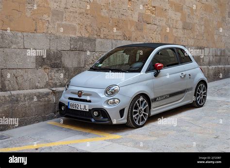 A Small White Modern Fiat Abarth Parked In A Street Near A Wall