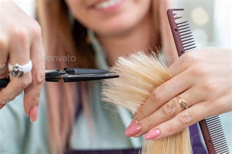 Hairdressers Hands Holding Scissors And Comb And Cutting Blond Hair Of