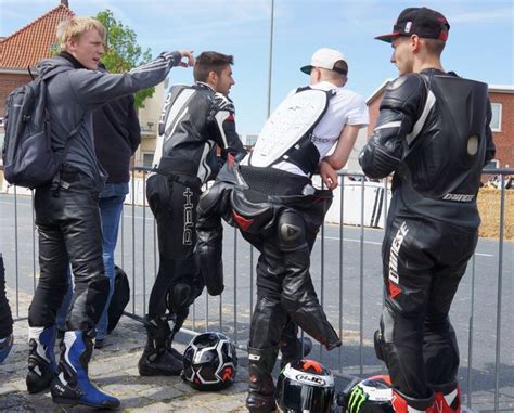 Four Men In Motorbikes Are Standing By A Fence And Talking To Each Other