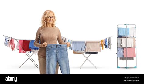 Mature Woman Holding A Pair Of Jeans In Front Of Clothes Drying On Racks Isolated On White