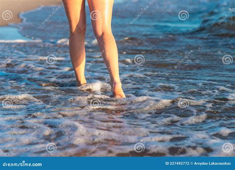 Pernas E Pés De Mulher Caminhando Sobre A Areia Da Praia Com água Do