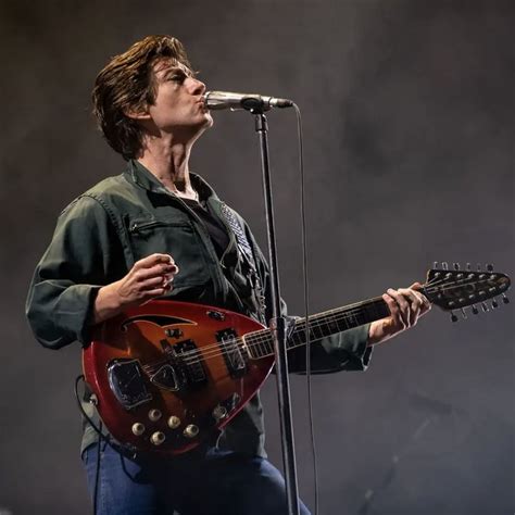 A Man Holding A Guitar While Standing In Front Of A Microphone