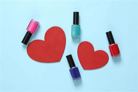 Botellas de esmalte de uñas y corazones rojos sobre fondo azul bodegón