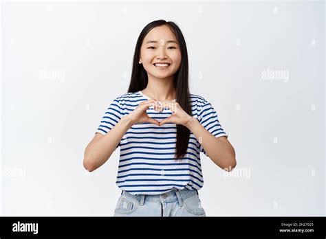 Romantic Asian Girl Shows Heart Sign And Smiles Happe At Camera Standing Over White Background