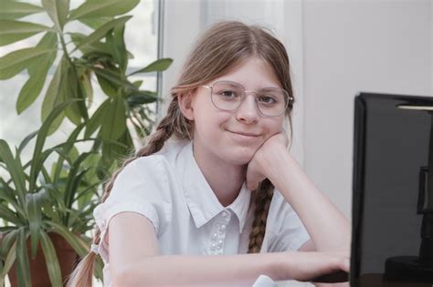 Premium Photo Smart Schoolgirl Does Homework Sitting At Her Desk Writes With A Pen In Her