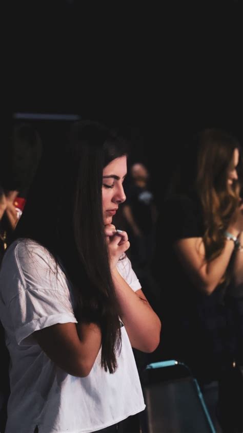 A Woman Standing In Front Of A Crowd With Her Hands Clasped To Her