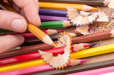 La mano sosteniendo el lápiz de color sobre un cuaderno con virutas de