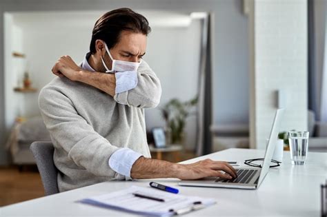 Joven empresario tosiendo en el codo mientras usa una máscara