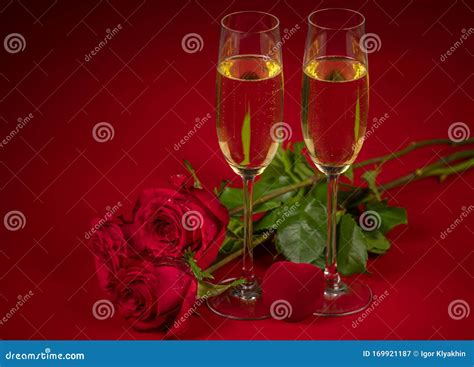 Red Roses Two Glasses Of Champagne And A Box In The Form Of A Red Heart On A Red Background In