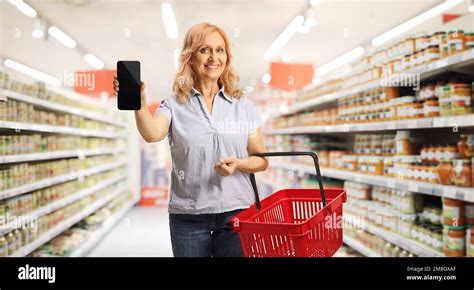 Smiling Mature Woman With A Red Shopping Basket Holding A Smartphone