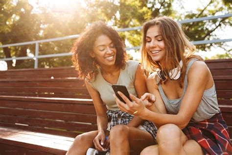 Deux Jeunes Filles Excitées Samusent Ensemble Tout En Utilisant Un Téléphone Portable Au Parc