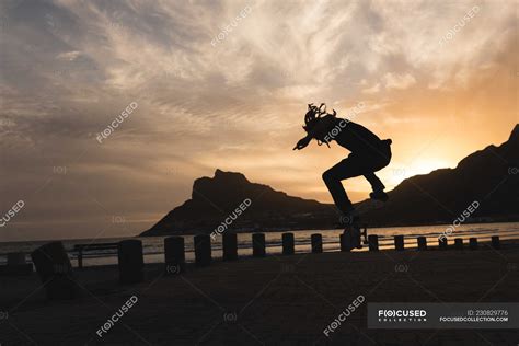 Silhouette of skateboarder skateboarding near beach during sunset ...