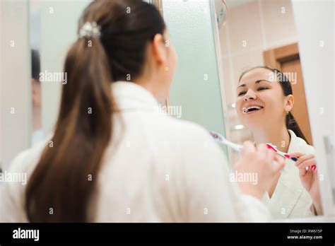 Image Of Pretty Female Brushing Her Teeth In Front Of Mirror In The