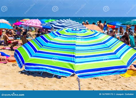 Colorful Beach Umbrella Stuck In The Sand Surrounded By A Group Of Bathers In Summer Near The