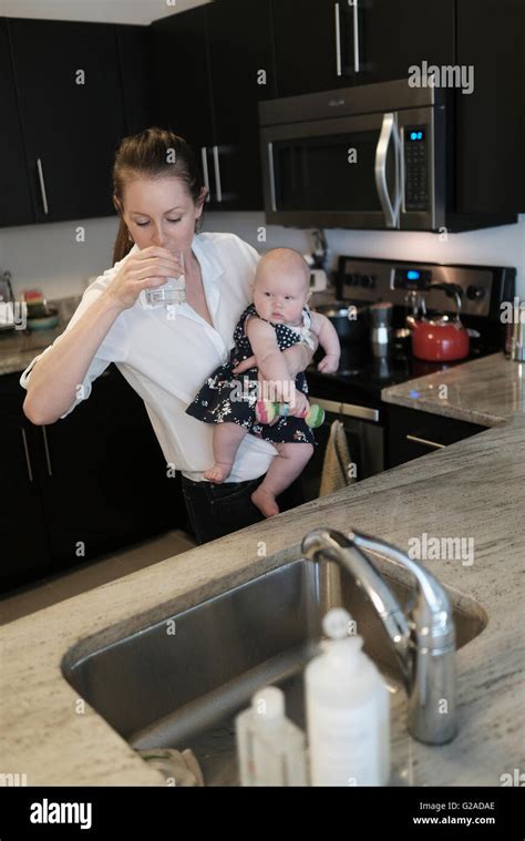 Mother drinking water while holding baby daughter (2-5 months Stock ...