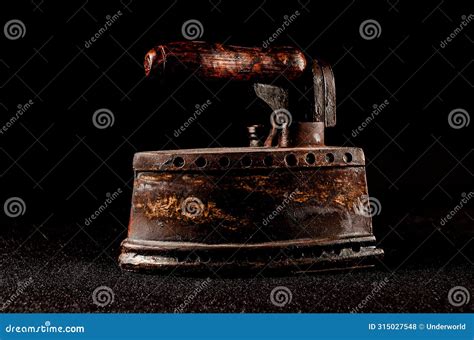 An Old Fashioned Iron With A Wooden Handle Sits On A Black Background