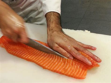 Chef Slicing A Raw Fresh Salmon Fillet With A Sharp Knife On A White