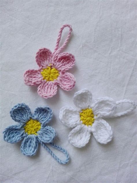 Three Crocheted Flowers Sitting On Top Of A White Cloth Covered Table