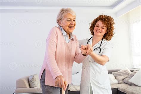 Enfermera Sonriente Ayudando A La Anciana A Caminar Por El Hogar De