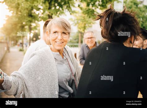 Portrait Of Smiling Mature Female Sitting With Friends And Enjoying At Social Gathering Stock