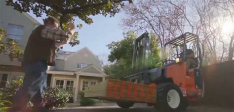 A Man Standing Next To A Tractor On A Driveway Near A House With Trees