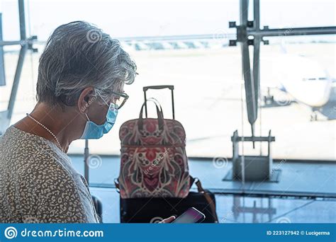 Senior Female Traveler Sitting In Airport With Luggages Using Mobile