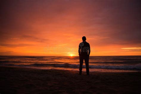 Hombre Solamente En La Playa Que Mira La Puesta Del Sol Foto De Archivo