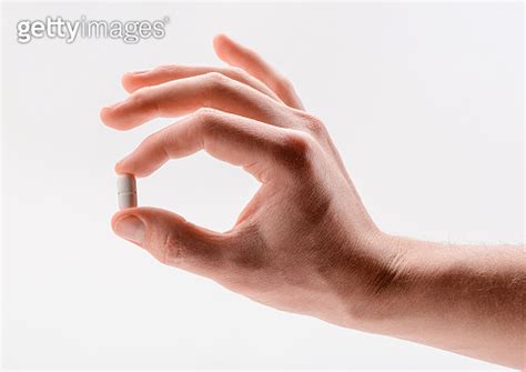 Hand Holding A White Caplet Pill Between Fingers