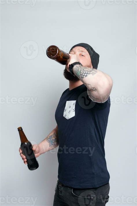 Brutal Bearded Male With Tattooed Arm Drinks A Beer From A Bottle