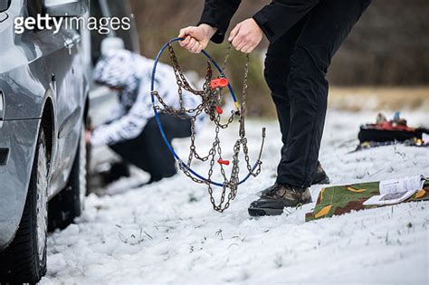 Adult Man Mounting Tire Chains on Car Tires on Country Road 이미지