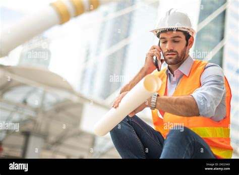 Caucasian Man Engineers Use A Smartphone For Talking Wearing An Orange