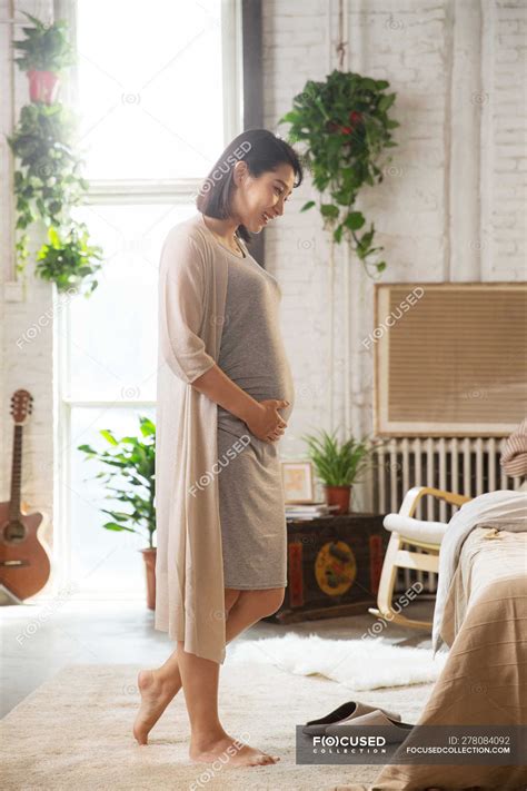 Side View Of Smiling Young Pregnant Woman Touching Belly At Home — Asian Woman Happy Stock