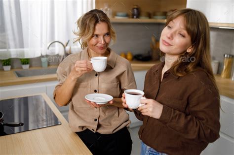 Cheerful Mother And Daughter Drinking Coffee In The Kitchen Together