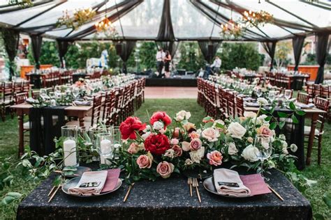 An Outdoor Tent Set Up For A Wedding Reception With Floral Centerpieces And Place Settings