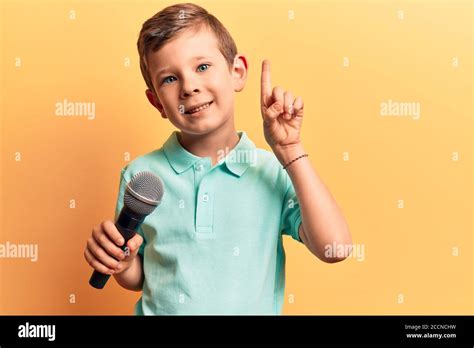 Cute Blond Kid Singing Song Using Microphone Smiling With An Idea Or