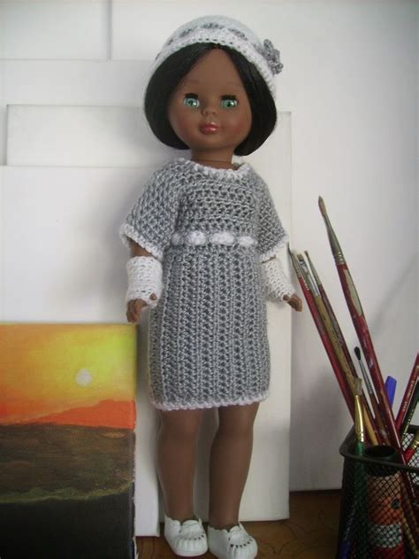 A Crocheted Doll Is Standing In Front Of A Painting And Some Pencils