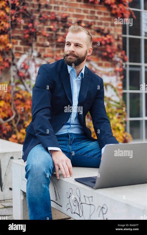 Bearded Young Handsome Man In Blue Blazer Sitting On Concrete Bench