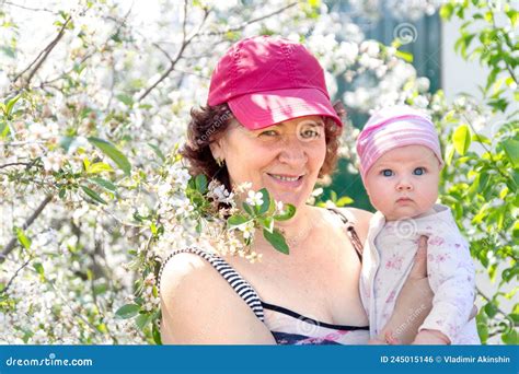 Grandmother Holds Her Little Granddaughter In Her Arms In A Blooming