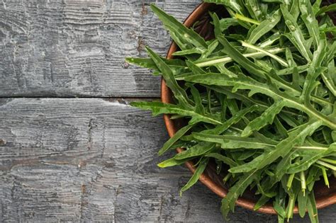 Hojas de rúcula verde fresca en un recipiente sobre una mesa de madera