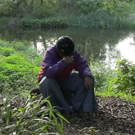 A Man Sitting On The Ground Next To A River Talking On A Cell Phone