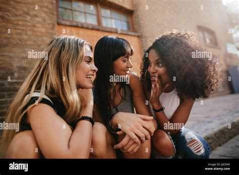 Shot Of Three Beautiful Girls Sitting Outdoors By The Road And Gossiping Female Friends