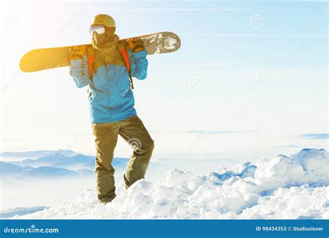 Young Snowboarder In Helmet Standing At The Top Of A Mountain With Sun